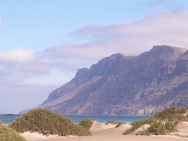 Plaj ve Dağlar - Caleta de Famara 'nın güzel kıyıları, Lanzarote Kanarya Adaları. Caleta de Famara 'daki plaj sörfçüler arasında çok popüler..