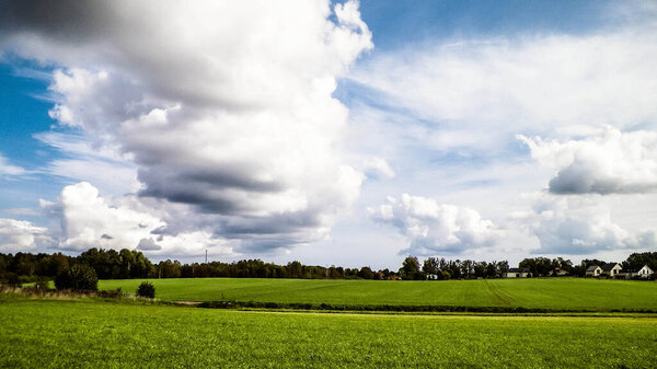Green field in the Kashubian countryside. Poland. Nature and agriculture concept. Copy space on cloudy sky.
