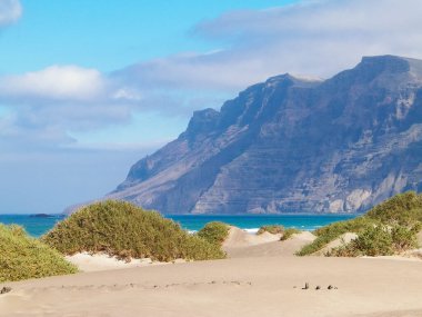 Plaj ve Dağlar - Caleta de Famara 'nın güzel kıyıları, Lanzarote Kanarya Adaları. Caleta de Famara 'daki plaj sörfçüler arasında çok popüler..