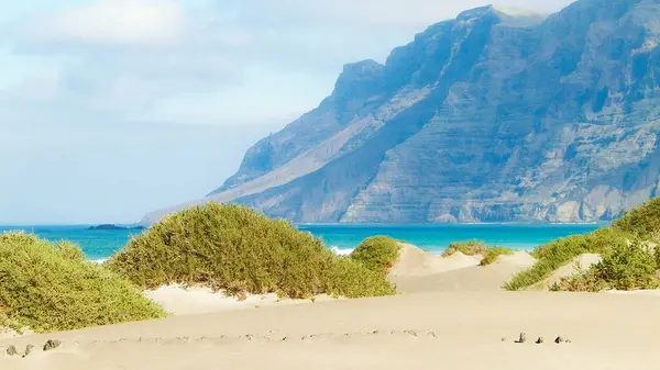 Plaj ve Dağlar - Caleta de Famara 'nın güzel kıyıları, Lanzarote Kanarya Adaları. Caleta de Famara 'daki plaj sörfçüler arasında çok popüler..