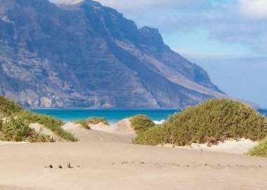Plaj ve Dağlar - Caleta de Famara 'nın güzel kıyıları, Lanzarote Kanarya Adaları. Caleta de Famara 'daki plaj sörfçüler arasında çok popüler..
