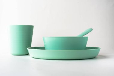 Plastik bardak, tabak ve beyaz arka planda izole edilmiş bir kaşık, çocuklar yeşil renkli plastik çatal bıçak takımı.