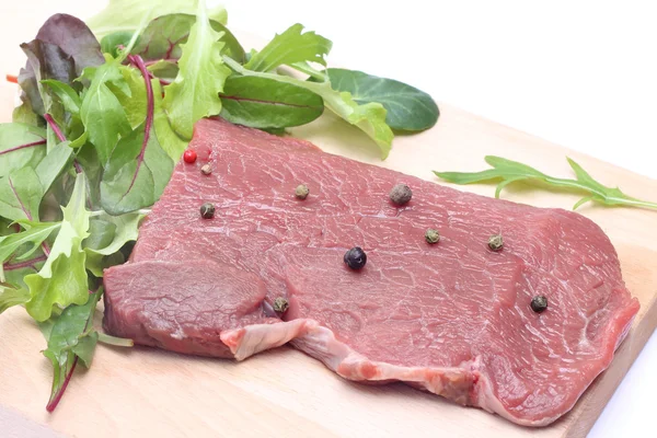 Ongekookt biefstuk op houten snijplank met salade — Stockfoto