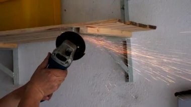 Bir işçi çeliği cilalamak için açı öğütücü kullanıyor. Her yerde kıvılcımlar uçuşuyor.