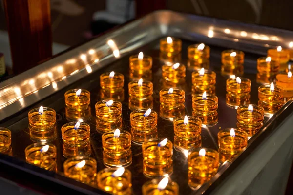 The tray is filled with lighted golden candles
