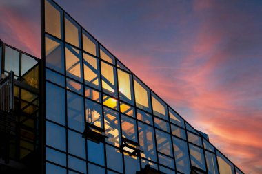 A corner of a modern building with a glass curtain wall in the sunset