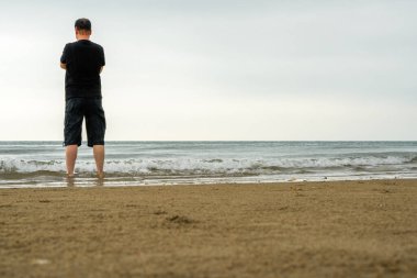 Uzun boylu Asyalı bir adam sahilde dikiliyor.