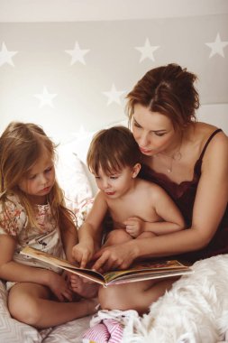 Annem yatakta küçük bir kız ve oğlana masal okuyor. Batı Highland beyaz teriyerinin yanında bir köpek