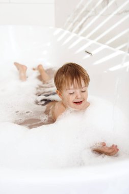 Küçük çocuk eğleniyor ve köpük banyosu yapıyor.
