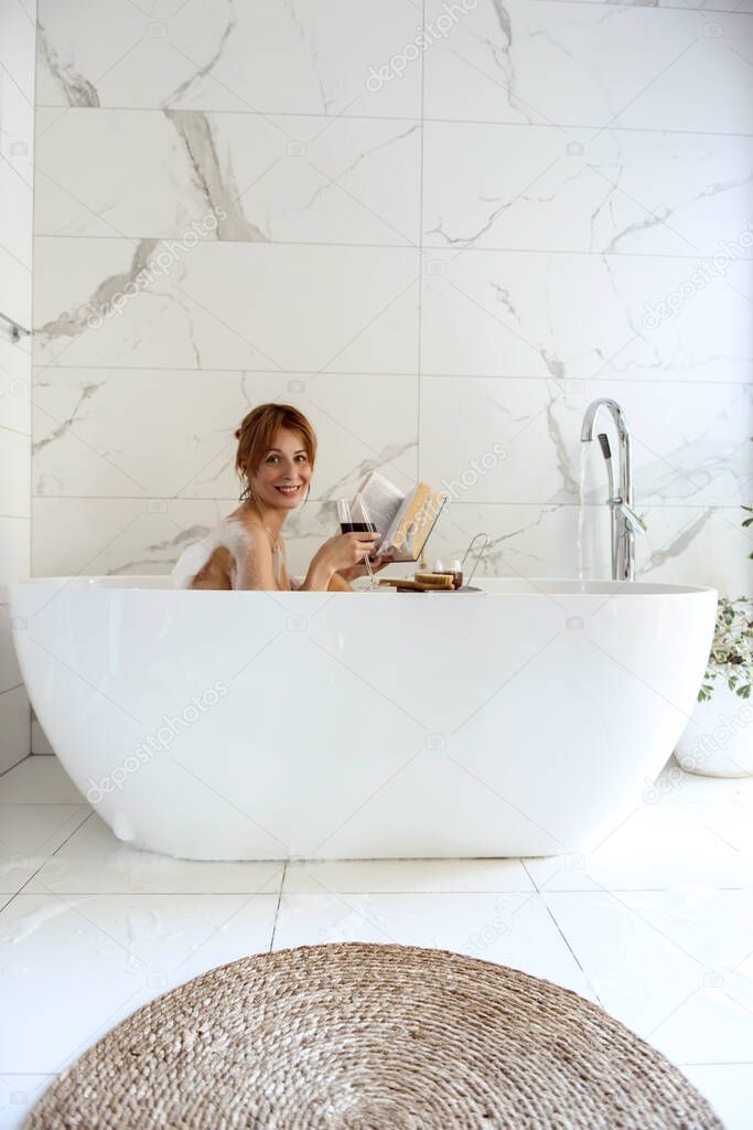 Woman lying in a bubble bath and drinking wine