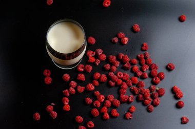 Bardaktaki süt ve siyah arkaplanda ahududu.