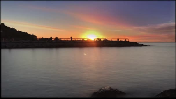 Silhuetter av människor och fiskare vid solnedgången på en brygga vid havet. — Stockvideo