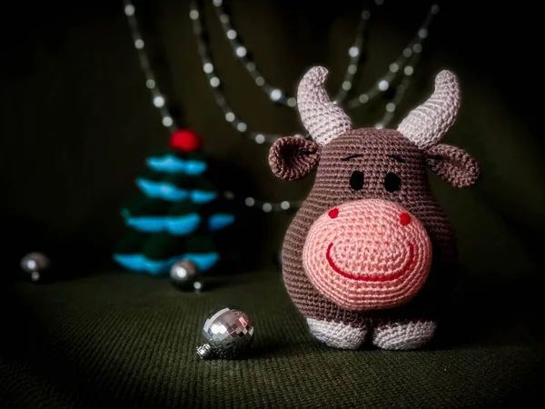 The symbol of the new year 2021. Knitted brown soft toy bull with horns. On green background and silver Christmas decorations. — Stock Photo, Image