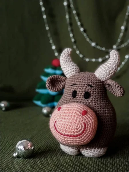 The symbol of the new year 2021. Knitted brown soft toy bull with horns. On green background and silver Christmas decorations. — Stock Photo, Image