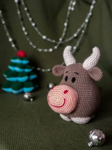 The symbol of the new year 2021. Knitted brown soft toy bull with horns. On green background and silver Christmas decorations. — Stock Photo, Image