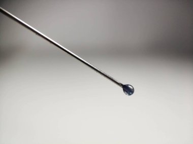 Şırınga iğnesinin ucunda bir damla var. Arka planda yakın plan.