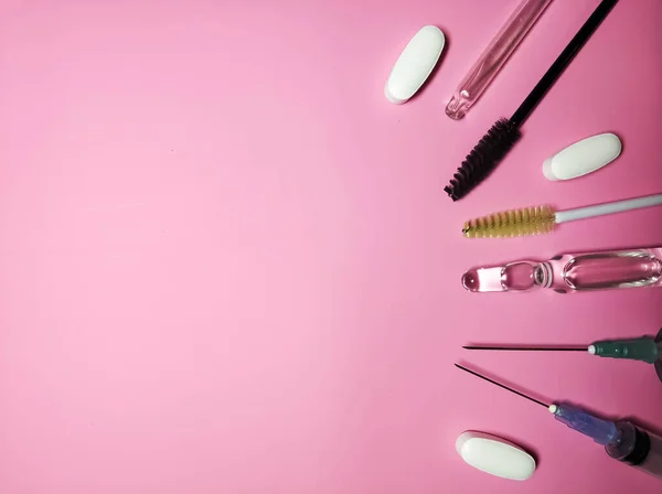 Medical cosmetology. Gloves, syringes, ampoule pills and brushes and eyebrows on a pink background side view — Stock Photo, Image