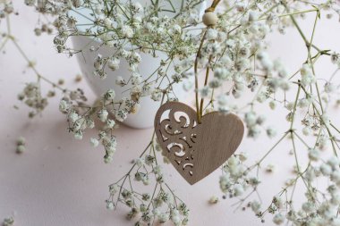 Tahta kalp ve beyaz porselen kupa. Hafif arka planda küçük beyaz çiçekler.