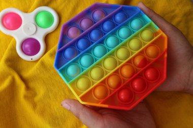 Çocukların elleri oyuncağı tutar, alkışlar. Stres önleyici. Gökkuşağı popüler bir silikon oyuncaktır. Sarı arka planda.