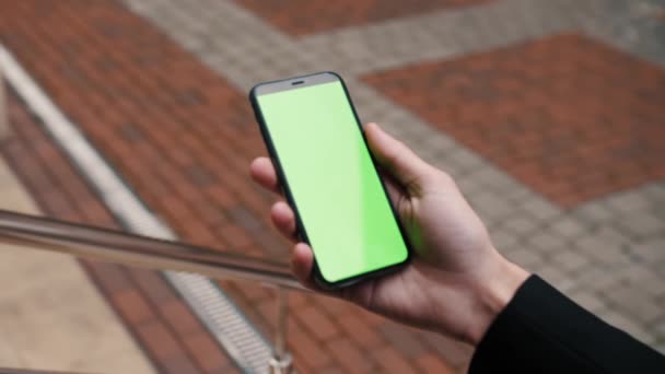 Vista de cerca de una persona que sostiene un teléfono inteligente deslizando páginas en la pantalla verde maqueta al aire libre. — Vídeos de Stock