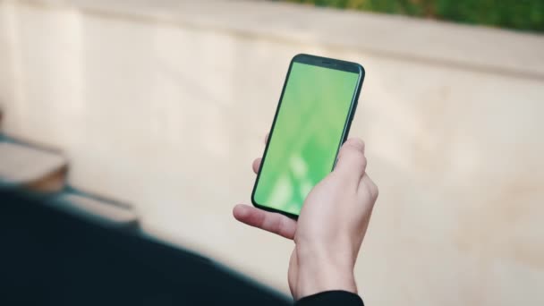 Over de schouder van de mens met behulp van een telefoon met een groen scherm buiten. Knappe man scrollen door smartphone apps buiten in de stad. — Stockvideo