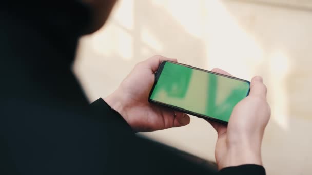 Mann benutzt Smartphone im horizontalen Modus mit grünem Bildschirm vor städtischem Geschäftsbüro — Stockvideo