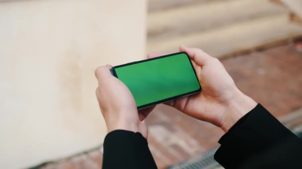 Man met behulp van Smartphone in horizontale modus met Green Mock-up Screen buiten de stad business office — Stockvideo