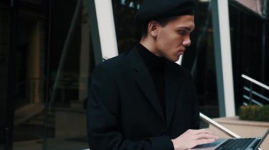Dışarıda merdivenlerde oturan yakışıklı genç işadamı laptopuyla çalışıyor.. 