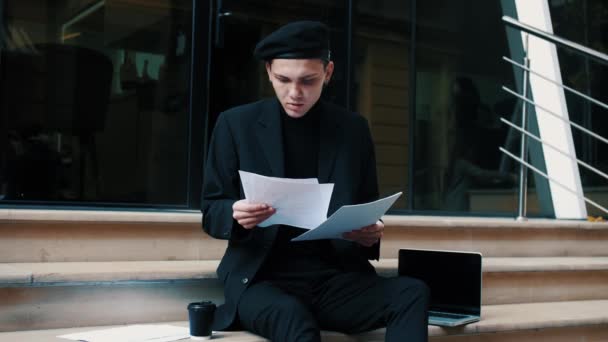 Hombre de negocios enfocado leyendo periódicos de negocios en una calle urbana. Hombre trabajando en las escaleras de la ciudad — Vídeo de stock
