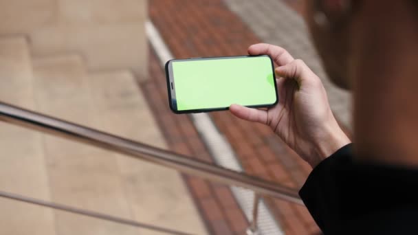 Mano masculina horizontal manteniendo la pantalla táctil teléfono inteligente ciudad urbana maqueta tapping pantalla verde cromakey exterior — Vídeo de stock