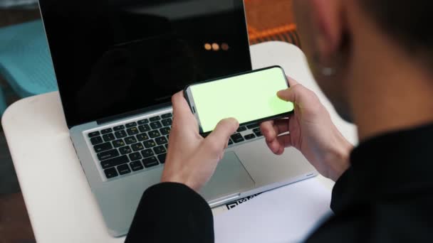 Homme utilisant un smartphone dans Coffee Shop. Smartphone avec écran vert en dehors de la ville urbaine — Video