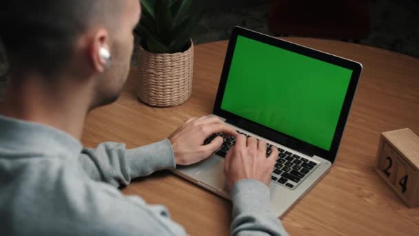 Joven hombre caucásico utilizando una pantalla verde portátil en el escritorio en casa. — Vídeo de stock