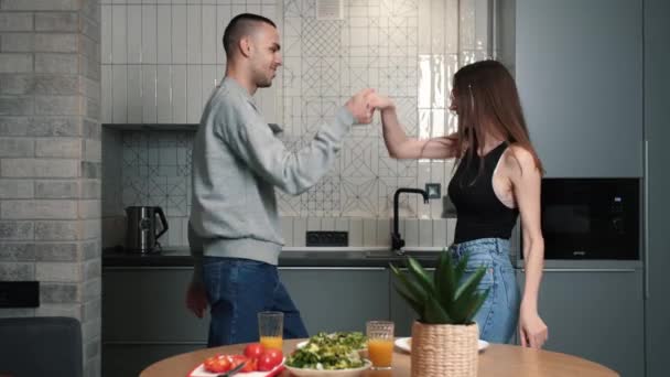 Młody szczęśliwy active family para taniec śmiejąc się razem przygotowując jedzenie w domu, beztroski radosny mąż i żona o zabawy gotowania i słuchać muzyki w nowoczesnej kuchni. — Wideo stockowe