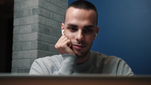 Primer plano sonriente hombre de negocios en auriculares inalámbricos ver la pantalla del ordenador portátil, funciona en la oficina en línea, utiliza el ordenador portátil. educación a distancia — Vídeo de stock