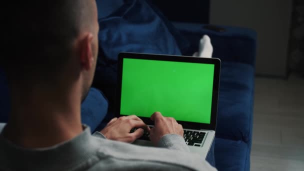 Mann mit Laptop und grünem Bildschirm entspannt sich auf dem Sofa. — Stockvideo