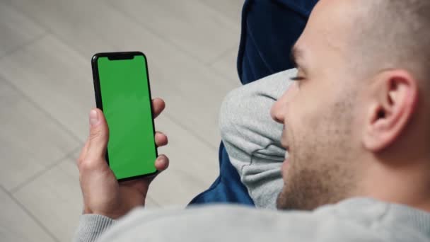 男はソファの上に横たわるクロマキー緑の画面でスマートフォンを使用して、インターネット、通信. — ストック動画