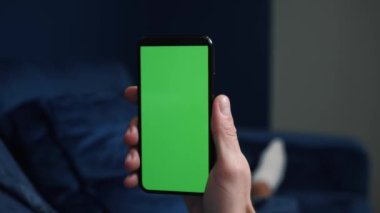 Close up shot of guy lying on couch at night, holding a smartphone with chroma key mock up green screen - technology, connections, communications concept 4k video template