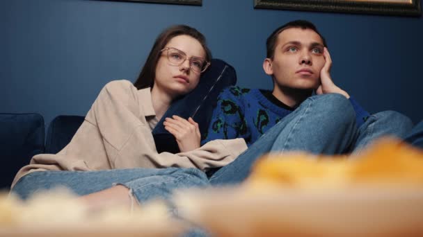 잘 생긴 젊은 백인 남녀가 집 소파에서 팝콘 과 함께 TV 에서 흥미 로운 영화를 보고 있다. — 비디오
