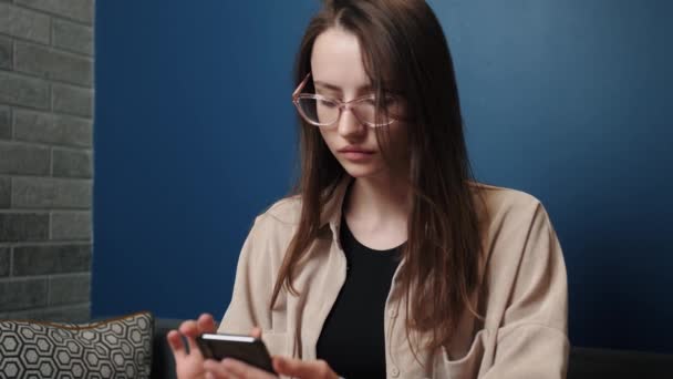 Atractiva joven mujer caucásica utilizar la plataforma de redes sociales telefónicas y sentarse en casa. permanecer en casa relajarse móvil sofá tecnología mensaje femenino interior en línea cámara lenta — Vídeo de stock