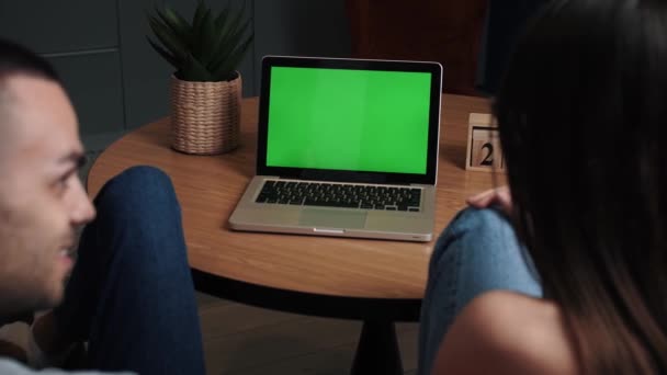 Junge Männer und Frauen im Home-Office-Geschäft mit grünem Laptop-Mock-up-Bildschirm, während sie auf der Couch im Wohnzimmer sitzen. Vergrößern Sie die Kamera aus der Rückansicht. — Stockvideo