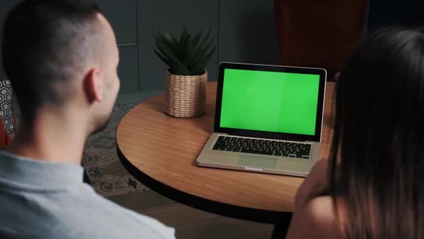 Junge Männer und Frauen im Home-Office-Geschäft mit grünem Laptop-Mock-up-Bildschirm, während sie auf der Couch im Wohnzimmer sitzen. Vergrößern Sie die Kamera aus der Rückansicht. — Stockvideo