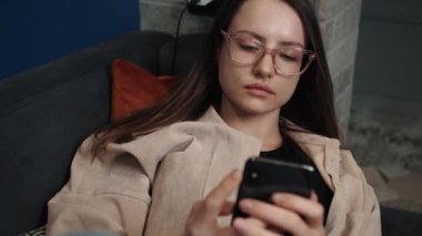 Çekici beyaz kadın telefon sosyal medya platformu kullanıyor ve evde oturuyor. Evde kal. Mobil kanepe teknolojisi. Kadın mesajları.