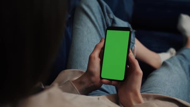 Woman hands holding smartphone mobile device with green display in home interior - over shoulder close up view. Mock up, chroma key, template, green screen, technology concept — Stock video