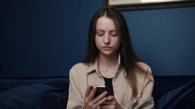 Çekici beyaz kadın telefon sosyal medya platformu kullanıyor ve evde oturuyor. Evde kal. Mobil kanepe teknolojisi. Kadın mesajları.