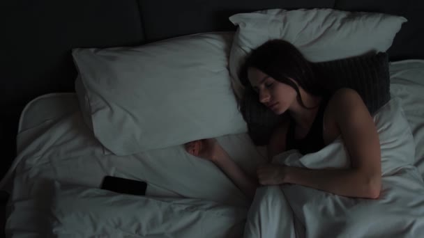 Vacker flicka sover i sängen hemma vaknar upp till inaktivera väckarklocka Triggade på sin telefon och vänder sig bort för att sova i Täckning upp i filt. Slow Motion Skott — Stockvideo