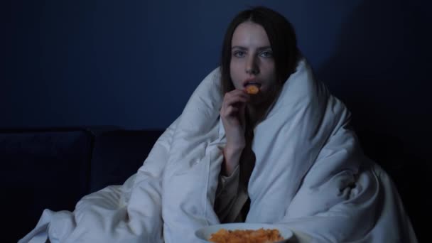 담요를 덮은 젊은 여자가 혼자 소파에 앉아 있습니다. TV 에 나오는 영화 — 비디오