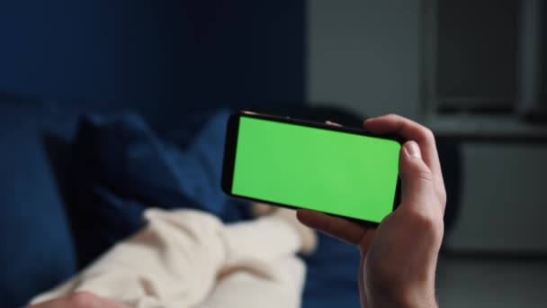 Hombre acostado en el sofá usando un teléfono inteligente con pantalla verde de croma por la noche, a través de las redes sociales, ver video, película o tienda en línea - Internet, concepto de comunicaciones de cerca. — Vídeo de stock