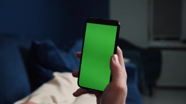 男人躺在沙发上，晚上用带有彩色键的绿色屏幕的智能手机，在社交媒体或网上商店里打转- -互联网，交流观念紧密相连. — 图库视频影像