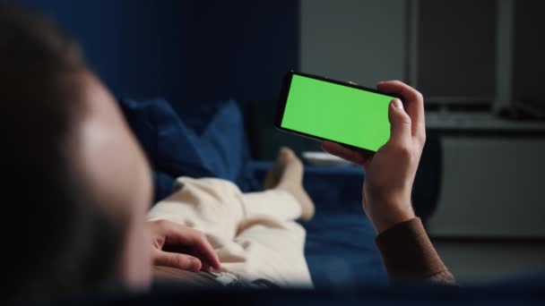 Homem deitado no sofá usando smartphone com tela verde croma chave à noite, através de mídias sociais, assistir vídeo, filme ou loja on-line - internet, conceito de comunicação de perto. — Vídeo de Stock