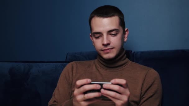 Zamknij kaukaski człowiek gra na telefonie i wygląda na skoncentrowany i szczęśliwy. Przystojny mężczyzna trzymający telefon poziomo i korzystający z niego leżąc w łóżku w domu. — Wideo stockowe